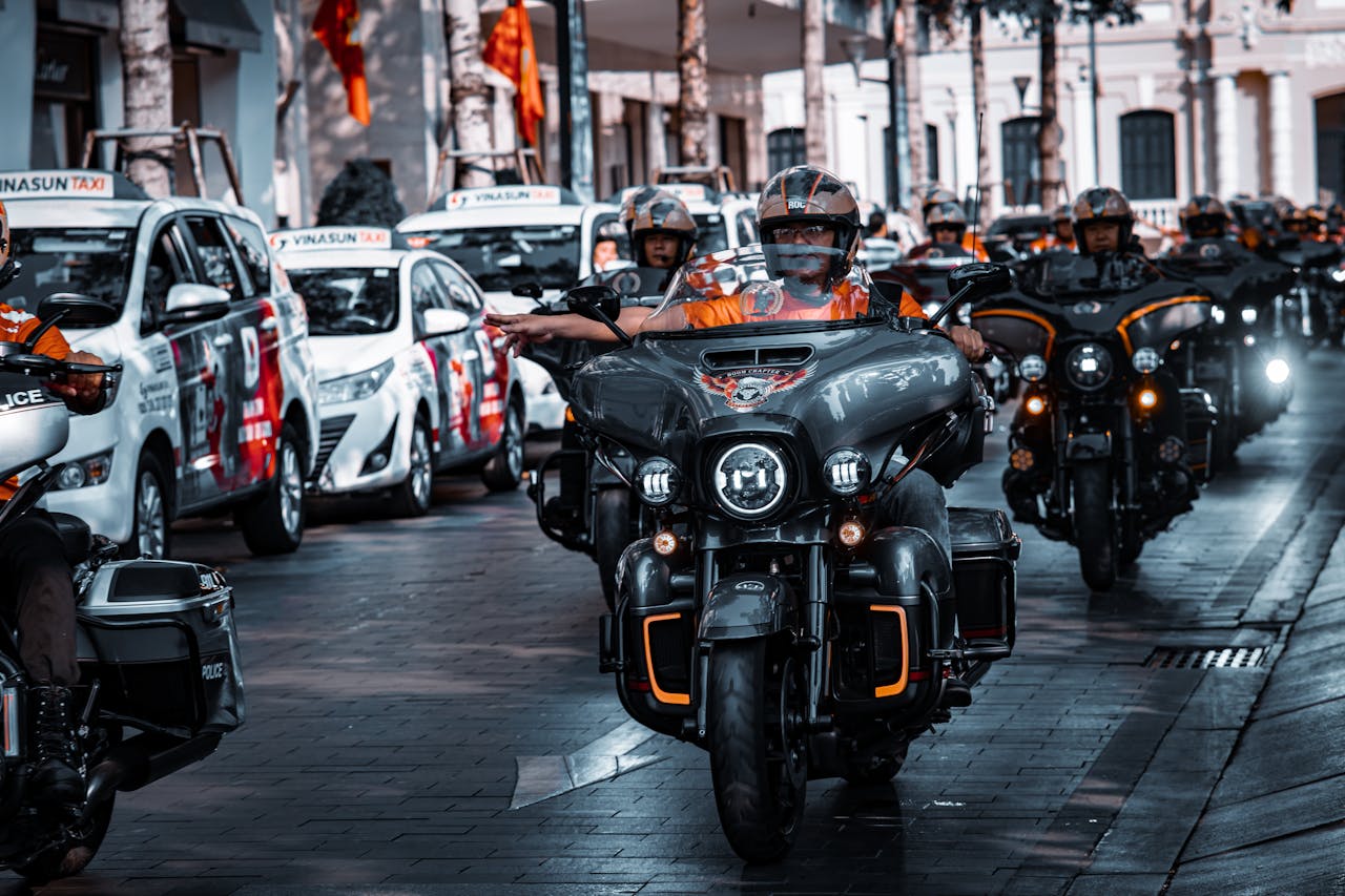 A group of bikers riding Harley-Davidson motorcycles on an urban street, captured in daylight.